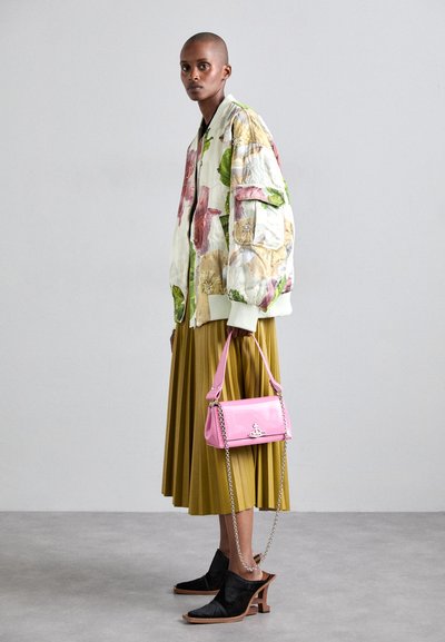 Giacca bomber floreale con sfumature verdi, rosa e gialle; gonna a pieghe color senape; piccola borsa rosa; mules nere con tacco e dettagli in legno.