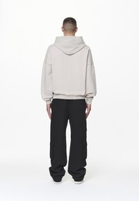 Ljusgrå oversized hoodie med en stor huva, i kombination med svarta cargobyxor som har sidfickor och en löst sittande design.