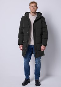 Černá péřová bunda s kapucí, s zipem a patentním uzávěrem, prošívaný design a boční kapsy, v kombinaci s modrými džíny a černými botami.