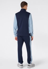 Chándal azul marino y celeste con cuello alto, que presenta una textura suave, mangas largas y puños y cinturilla elásticos. Zapatillas grises incluidas.