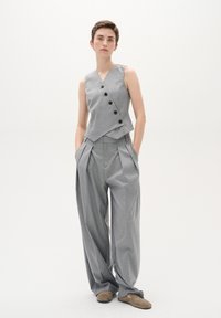 Grau kariertes Weste mit V-Ausschnitt und fünf Knöpfen, kombiniert mit locker sitzenden grauen Hosen mit Falten. Weicher Stoff, minimalistisches Design.