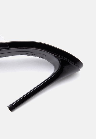 Μαύρο γυαλιστερό δερμάτινο πέδιλο με λεπτό στιλέτο και διαφανή λουρί σε λευκό φόντο.