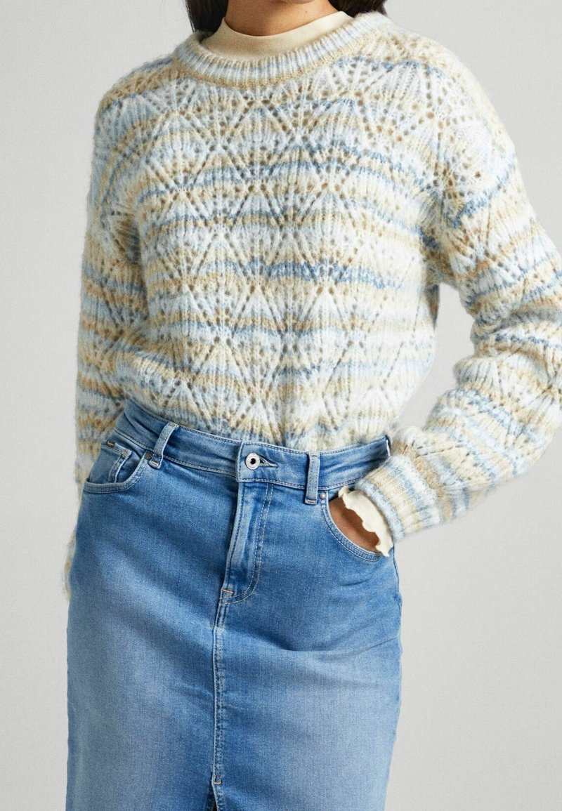 Maglione lavorato a maglia con motivo geometrico in blu chiaro, crema e beige; scollo rotondo e polsini a costine abbinati a una gonna di jeans.