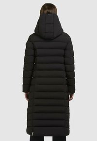Piumino nero con un design lungo e aderente, caratterizzato da cuciture orizzontali, cappuccio e dettagli con tasca laterale con zip.