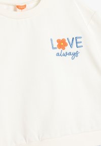 Vit baby sweatshirt med broderad text "LOVE" i blått och en orange blomdetalj, rund halsringning och elastisk midja.