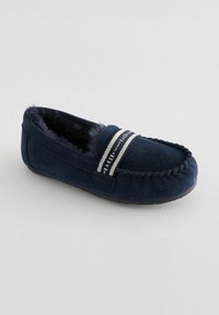Pantofole in suede blu navy con fodera in pelliccia sintetica, cuciture decorative e una fascia a righe sulla parte superiore con il testo del marchio. Design con suola piatta.