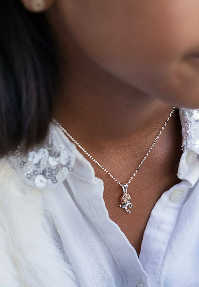 Silverhalsband med en ros i rosa och silvertoner, bärs över en vit skjorta med krage dekorerad med paljetter.