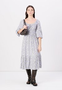 Rochie florală de un mov deschis, cu mâneci bufante și fustă în clărimi. Purtată cu cizme din piele maro până la genunchi și o geantă mică neagră.