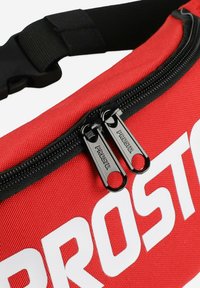 Czerwona torba na ramię z gładką powierzchnią, czarnym zamkiem błyskawicznym i dużymi białymi literami. W zestawie regulowany czarny pasek.