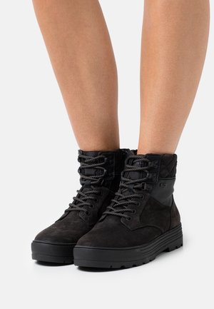 Botas de tobillo de ante negro con cuello textil acolchado, cordones texturizados y suela de goma gruesa. Cuenta con ojetes de metal y acentos de logo.