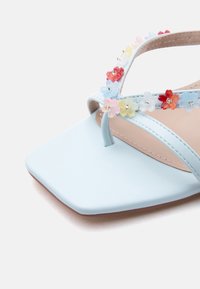 Ανοιχτό γαλάζιο σανδάλι με τετράγωνη μύτη, διακοσμημένο με πολύχρωμες διαφανείς ανθοστολίδες κατά μήκος των λουριών.