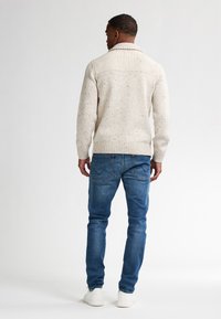 Valkoinen neulepusero, jossa on ribattu kaulus ja tekstuuri. Yhdistettynä sinisiin farkkuihin ja valkoisiin tennareihin, nähtynä takaa.