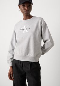Gray cotton sweatshirt with a crew neckline, ribbed cuffs, and hem. Features a white logo reading "Calvin Klein" in the center.