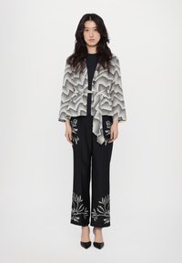 Outfit in bianco e nero composto da una giacca a fantasia con cintura e pantaloni a gamba larga con ricami floreali all'orlo. Tacchi a spillo completano il look.