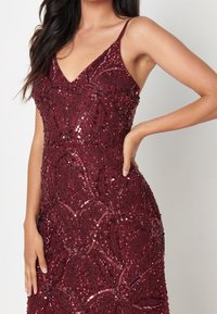 Burgundy iltapuku ohutolkaimilla, joissa on monimutkaisia helmi- ja paljettikuvioituneita kukkia sekä istuva siluetti, joka korostaa teksturoidun pinnan.