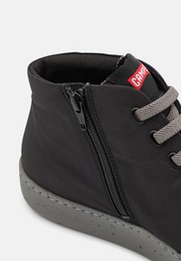 Pantof inflat negru, realizat dintr-un material texturat, având un fermoar pe lateral, șireturi gri și o talpă din cauciuc gri cu pete. Accent logo roșu pe limbă.