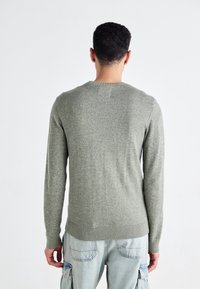 Grön stickad tröja med långa ärmar, ribbade cuffs och fåll. Tyget har en subtil struktur och är figursydd vid midjan.