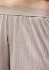 Κοντινή λήψη σε μπεζ ριμπ ύφασμα σορτς με ελαστική μέση που φοριέται στη μέση ενός ατόμου.