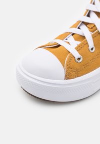 Yellow canvas sneaker with a white rubber toe cap, flat laces, and a textured rubber sole. Features silver eyelets and stitched accents.