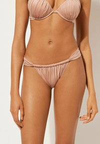 Blush-pink Bikini-Oberteil mit gefälteltem Design und Bügel, kombiniert mit passende minimalistischem Unterteil mit gerafften Seitendetails.