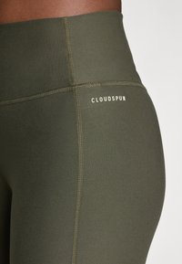 Olivi vihreät korkeavyötäröiset leggingit, jotka on valmistettu joustavasta kankaasta. Niissä on litteät saumat ja vaaleankermanvärinen "CLOUDSPUN" -logo.