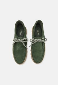Scarpe in suede verde con una finitura testurizzata, dotate di una suola in gomma e lacci a motivo contrastante. Progettate in stile mocassino.