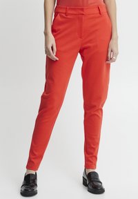 Red fitted trousers with a smooth texture, featuring a flat front and belt loops. Paired with black patent shoes for contrast.