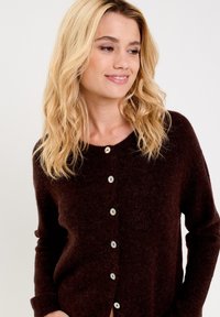 Cardigan marrone, morbido, con maniche lunghe e scollatura rotonda. Presenta cinque bottoni chiari lungo la parte anteriore e una vestibilità comoda.