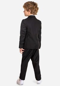 Black suit with a jacket and trousers, featuring a white shirt and white sneakers. Smooth texture, tailored fit, and classic design.