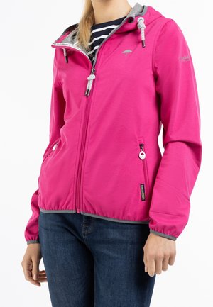 Kobieta ubrana w jaskraworóżową kurtkę zapinaną na zamek z szarymi wykończeniami i dwoma kieszeniami na zamek, w połączeniu z ciemnoniebieskimi dżinsami.