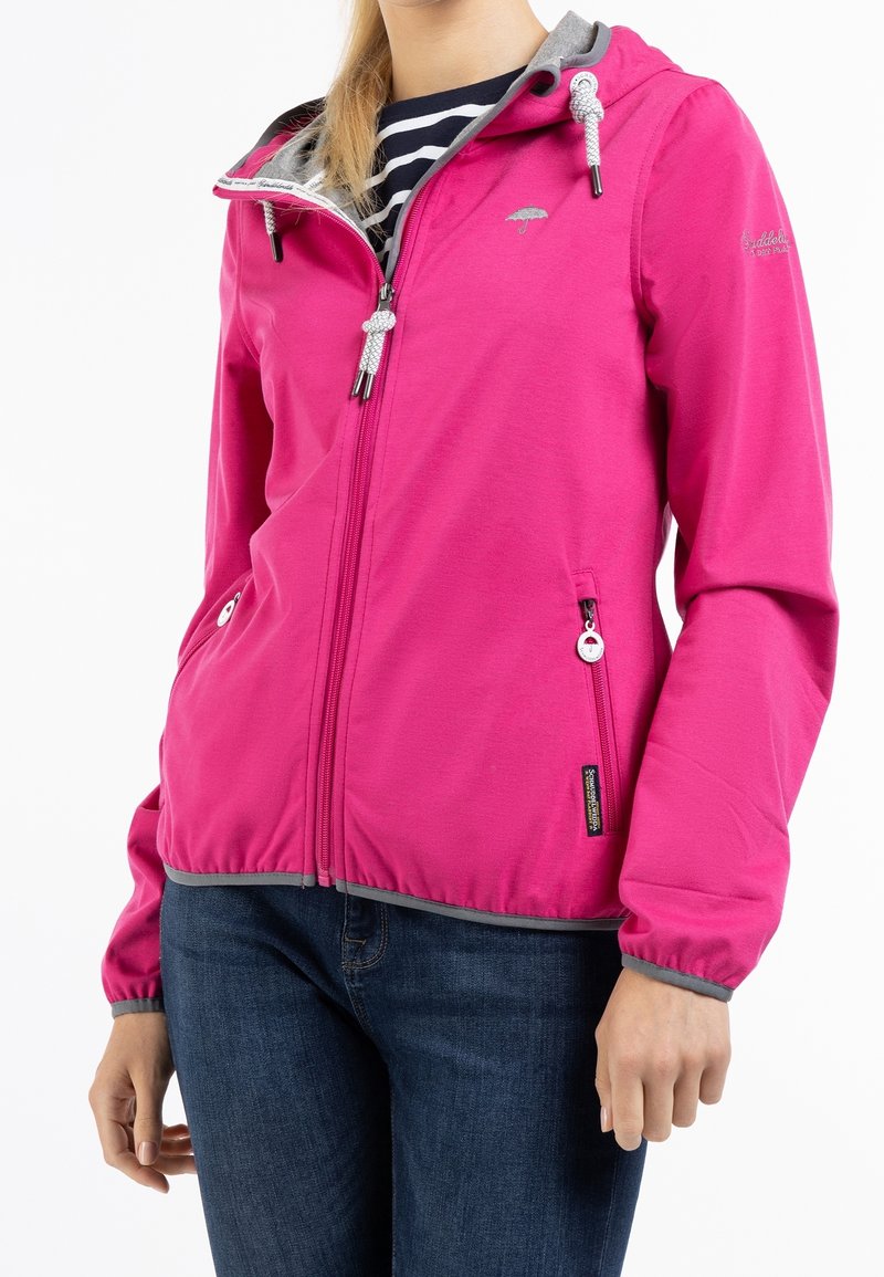Femme portant une veste zippée rose vif avec une bordure grise et deux poches zippées, associée à un jean bleu foncé.