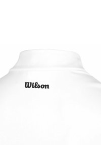 Chemise polo blanche avec un logo noir "Wilson" au dos, col classique et tissu lisse et texturé.