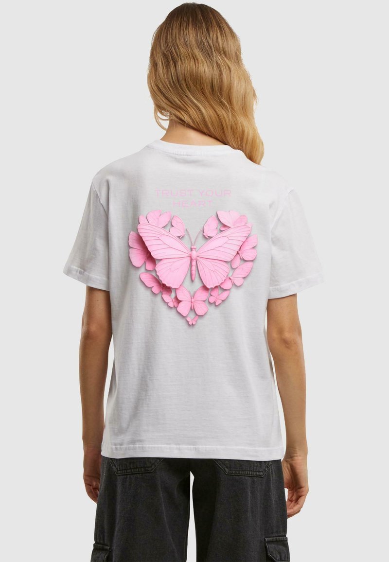 Weißes T-Shirt mit kurzen Ärmeln, das ein 3D-Rosa-Schmetterlings- und Blumenmuster auf dem Rücken zeigt, mit dem Text "Vertraue deinem Herzen" darüber.