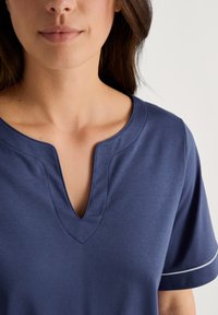 Navyblauw T-shirt met korte mouwen en een V-hals, afgewerkt met contrasterende witte stiksels langs de mouwen, vervaardigd uit een gladde, zachte stof.