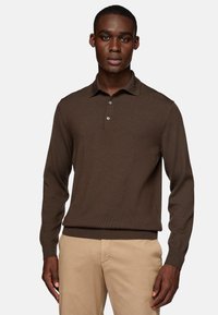 Camisa de polo marrón de manga larga con una textura acanalada, tapeta de tres botones y cuello con solapa, combinada con pantalones beige claro.
