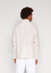 Camicia leggera a righe in beige e crema, con maniche lunghe, colletto alla francese e vestibilità morbida. La trama del tessuto sembra morbida.