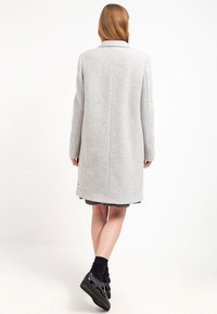 Szary wełniany płaszcz o prostym kroju, z kołnierzem z wcięciem i przeszywanym tyłem. Posiada długie rękawy i sięga do kolan.
