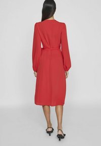 Červené midi šaty s dlhými rukávmi a opaskom v páse. Vyrobené z hladkej látky s voľným strihom a manžetovými rukávmi, s okrúhlym výstrihom.