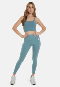 Sujeción deportiva turquesa y leggings de cintura alta, fabricados con tejido elástico. Presenta un acento de logo y un diseño ajustado, combinados con zapatillas blancas.