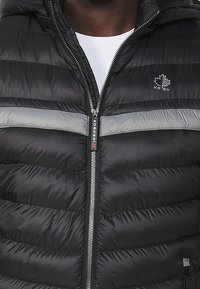 Black puffer jacket with a hood, featuring horizontal quilted panels, a gray stripe across the chest, and a front zipper with branded pull tab.