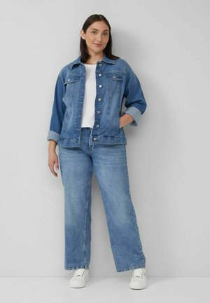 Denimjacke und lässige Jeans mit weitem Bein in einem hellblauen Farbton, mit Knopfverschlüssen und hochgekrempelten Ärmeln, kombiniert mit einem weißen T-Shirt und Sneakers.