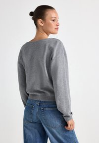Grijze trui met een relaxed fit, geribbelde zoom en mouwen, en een brede halslijn. Gecombineerd met hoge taille blauwe denim jeans.