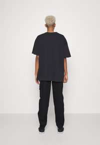 T-shirt nera oversize con maniche corte, abbinata a pantaloni cargo neri con tasche laterali. Tessuto morbido, vestibilità comoda, design basic.