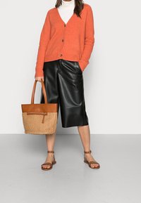 Orangeknitted cardigan, vit polotröja, svarta fusk läder culottes, brun vävd totebag med läderdetaljer, och bruna sandaler.