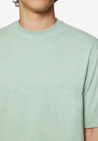 Világoszöld, rövid ujjú póló, puha anyagból készült, kerek nyakkivágással és sima, egységes textúrával.