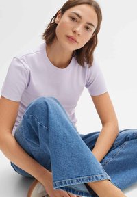 Lila T-shirt met korte mouwen en een ronde hals, gemaakt van zacht materiaal. Gecombineerd met hoge wijde blauwe spijkerbroeken, met een klassieke denimstructuur.