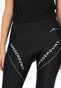 Black bike shorts made of a stretchy material, featuring white "SWEDEMOUNT" branding and reflective accents along the seams.