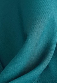 Teal fabric with a smooth texture, featuring a subtle sheen and diagonal weave pattern, folded to create gentle curves and soft drapes.