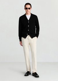 Cardigan noir en tricot avec col en V, orné de boutons argentés, associé à un pantalon crème clair et des mocassins noirs. Des lunettes de soleil complètent la tenue.