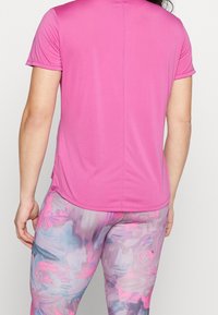 Camiseta deportiva ajustada de manga corta en color rosa con textura suave, combinada con leggings coloridos de patrones abstractos en tonos pastel.